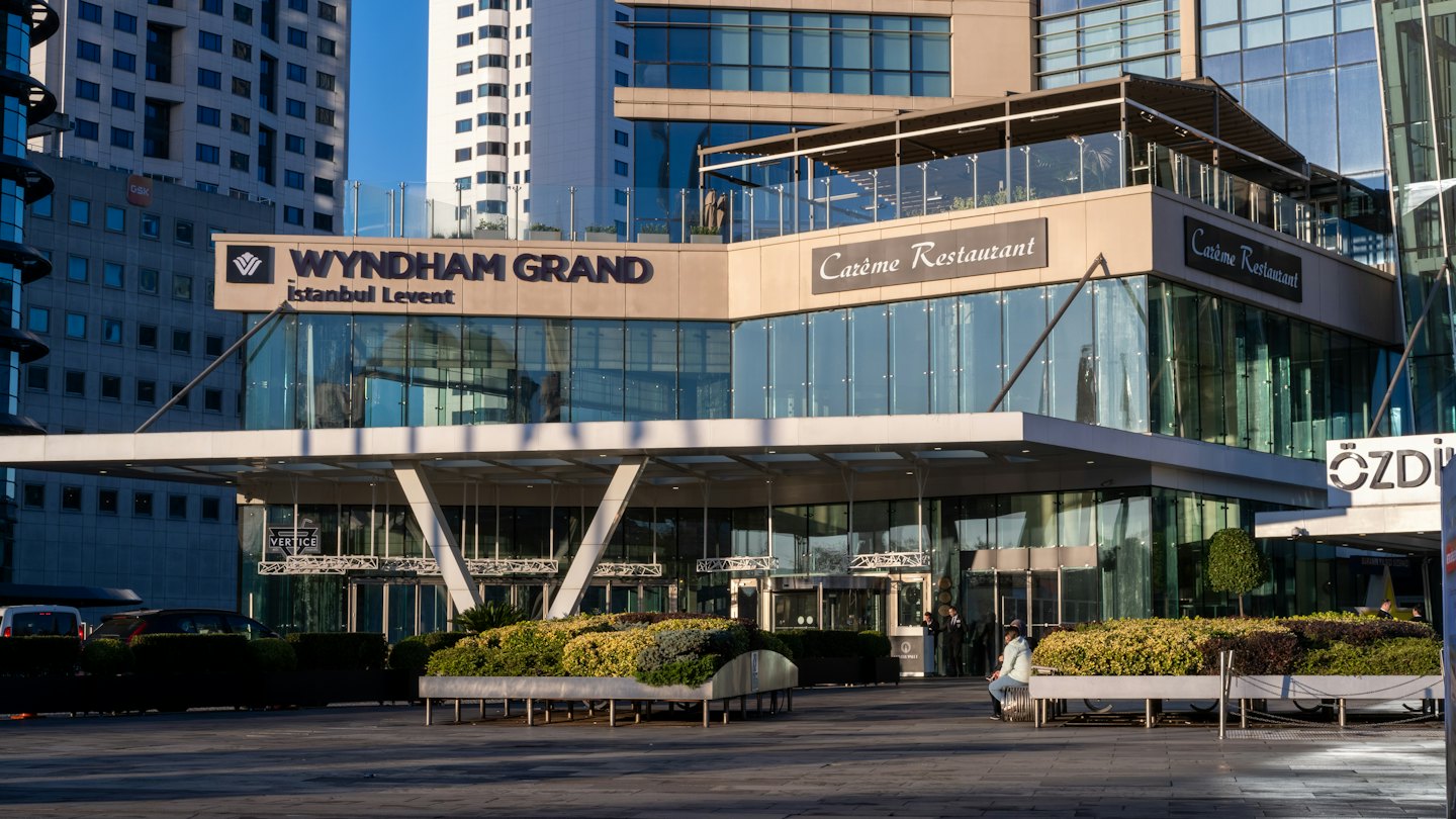 Tabela ve bankta oturan bir kişinin olduğu modern otel binası.
